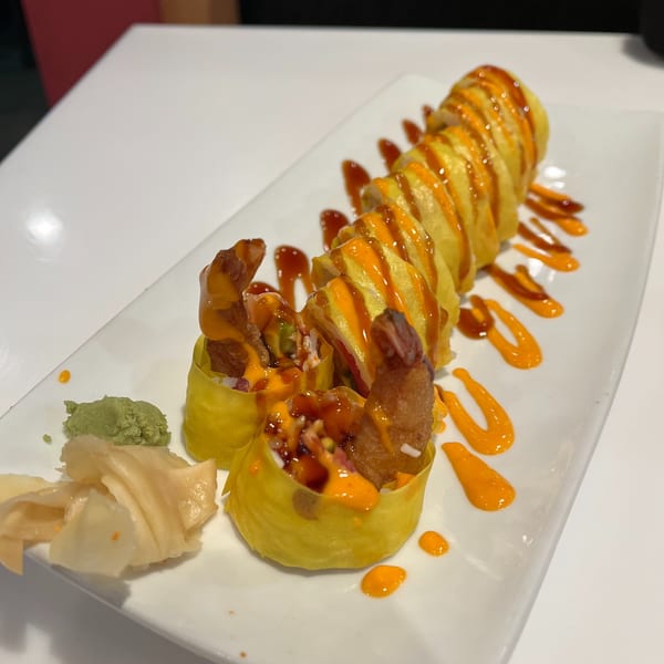 Asian-fusion sushi rolls with fried shrimp, drizzled with orange and brown sauces, served with ginger and wasabi.