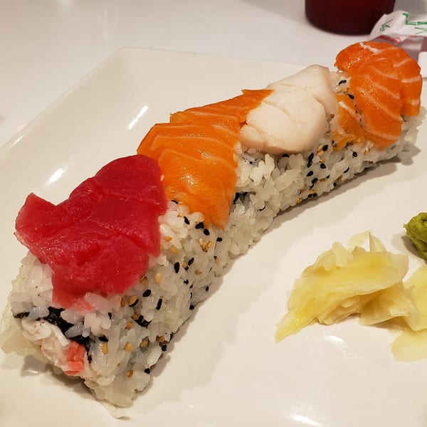 A long sushi roll topped with tuna, salmon, and white fish, served with ginger and wasabi.