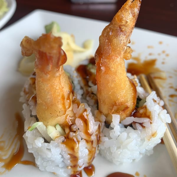 Two pieces of tempura shrimp sushi rolls with sauce drizzled over them, served on a white plate.