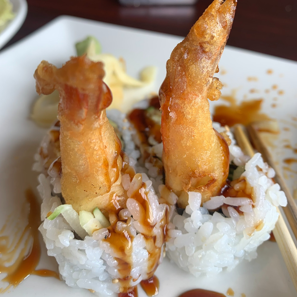 Two pieces of tempura shrimp sushi rolls with sauce drizzled over them, served on a white plate.