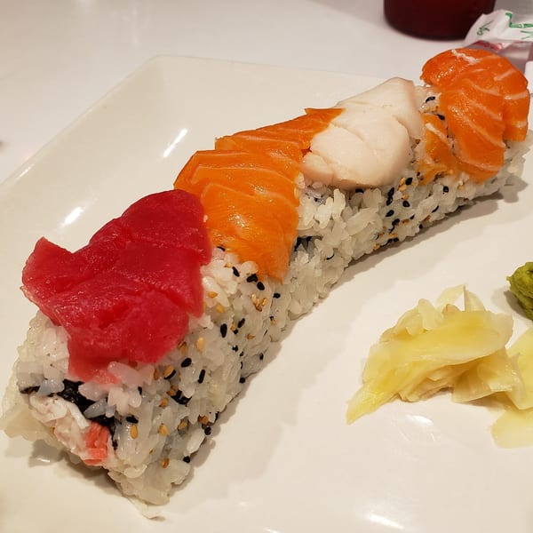 A long sushi roll topped with tuna, salmon, and white fish, served with ginger and wasabi.