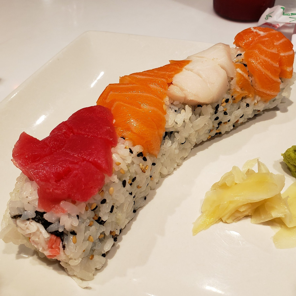 A long sushi roll topped with tuna, salmon, and white fish, served with ginger and wasabi.