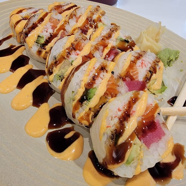 A plate of Lim Dynasty sushi rolls with various fillings, drizzled with spicy mayo and eel sauce.