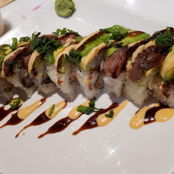 Lim Dynasty Asia Cafe & Xpress's sushi roll topped with beef, avocado, green onions, and sauces.